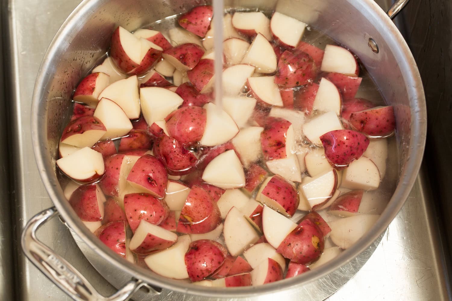 Chopped red potatoes in a pot being covered with water.