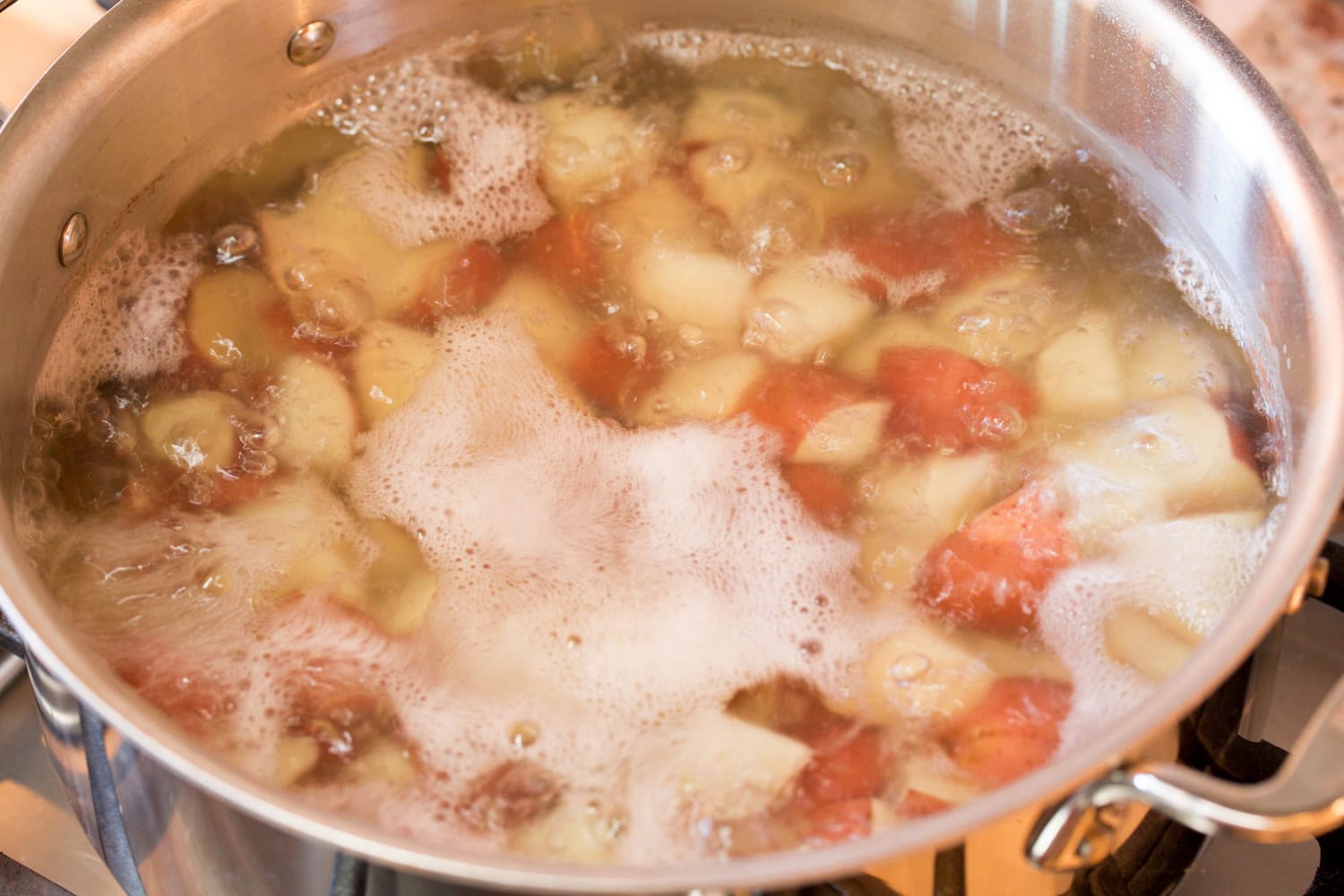 Chopped red potatoes being boiled on the stove in a pot.