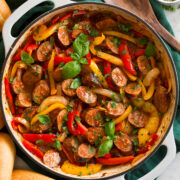 Sliced Italian sausage, peppers and onions in a skillet. Shown with hoagies to the side as a serving suggestion.