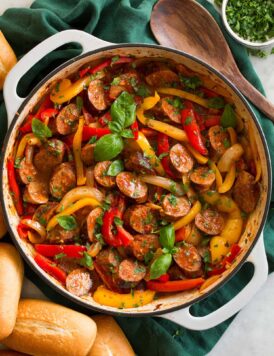 Sliced Italian sausage, peppers and onions in a skillet. Shown with hoagies to the side as a serving suggestion.