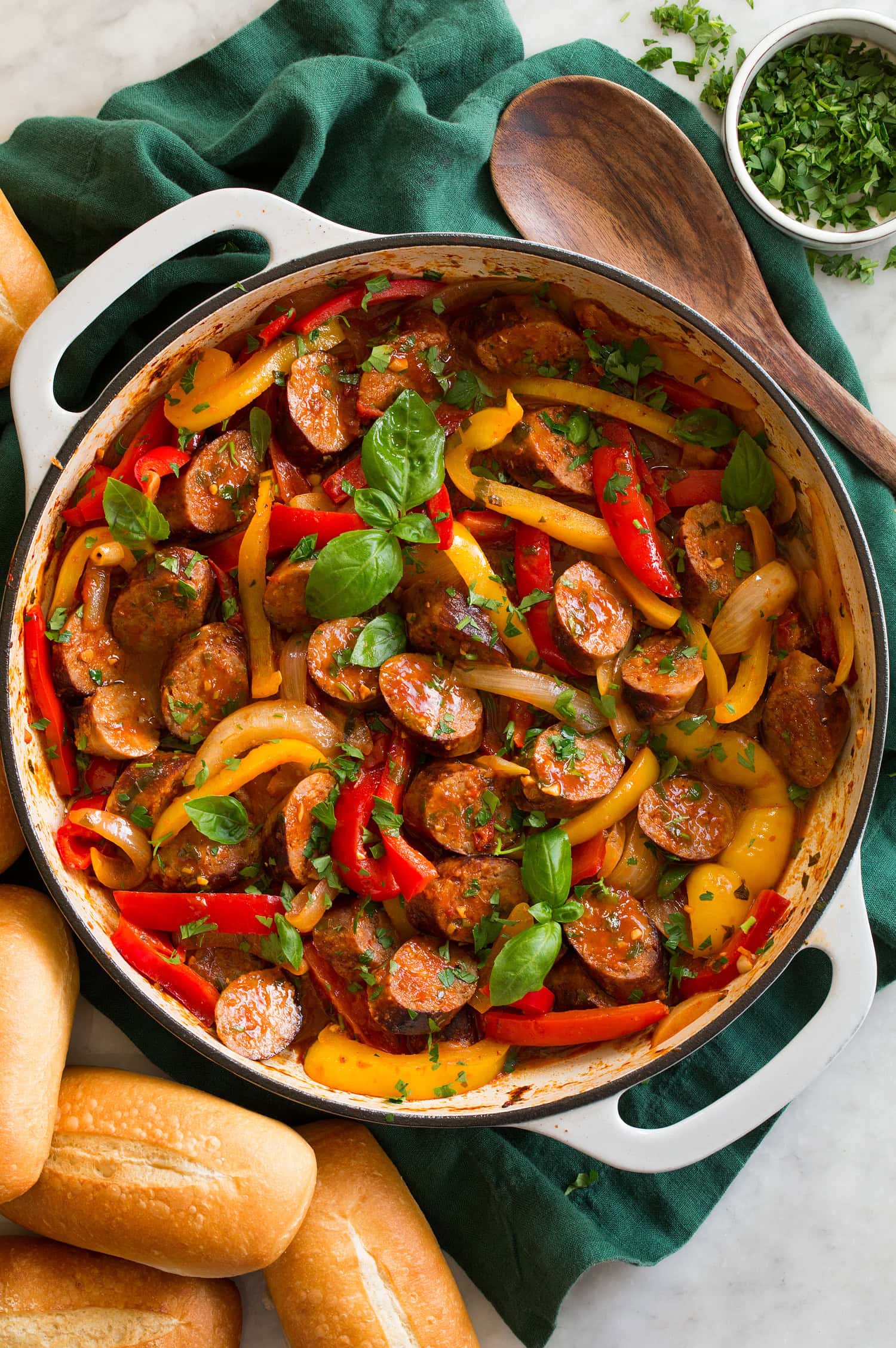 Sliced Italian sausage, peppers and onions in a skillet. Shown with hoagies to the side as a serving suggestion.