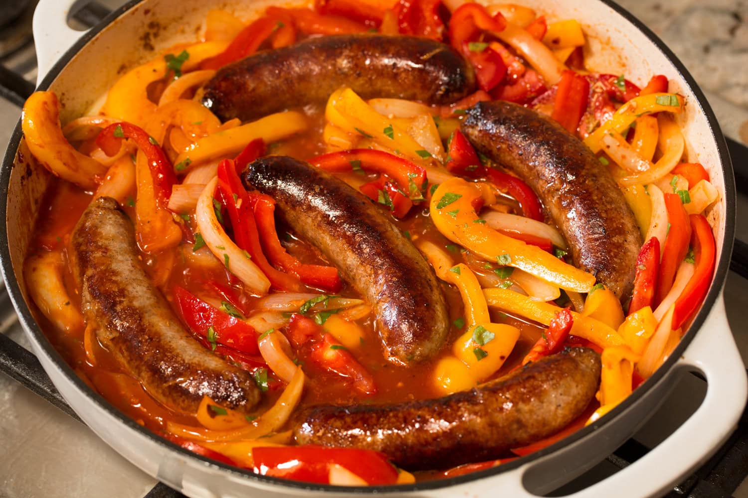 Browned sausages shown nestled into pepper and onion mixture in pan.