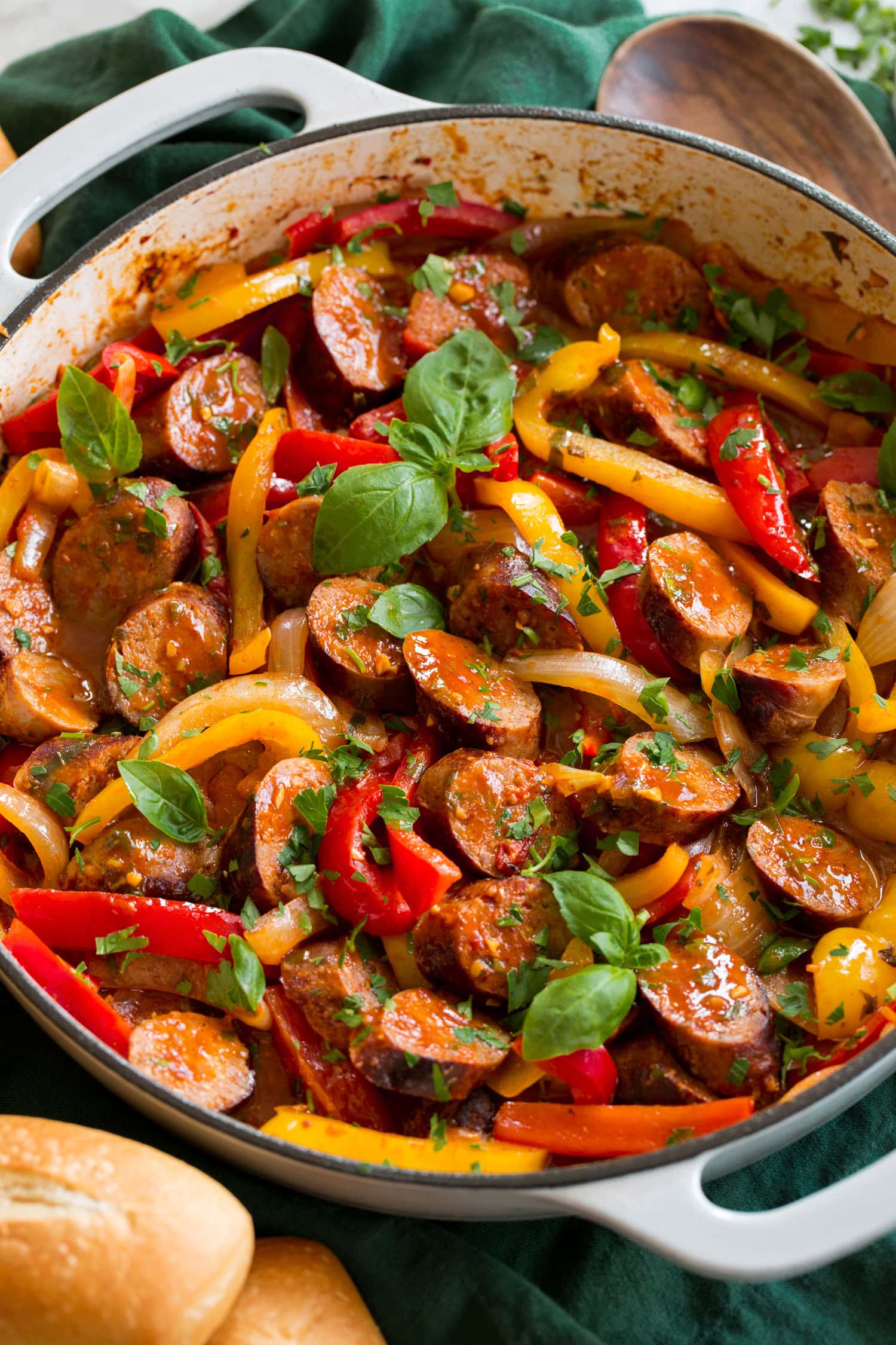 Sausage, peppers and onions shown close up in a white enameled skillet.