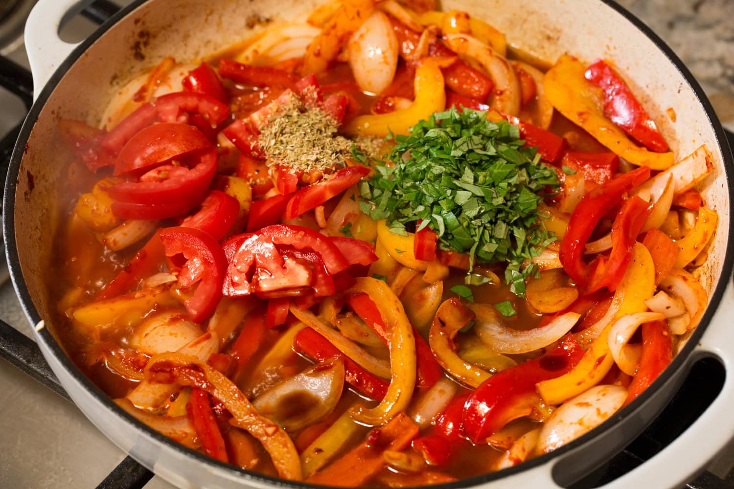 Tomatoes, basil and oregano added to sauteed peppers mixture.