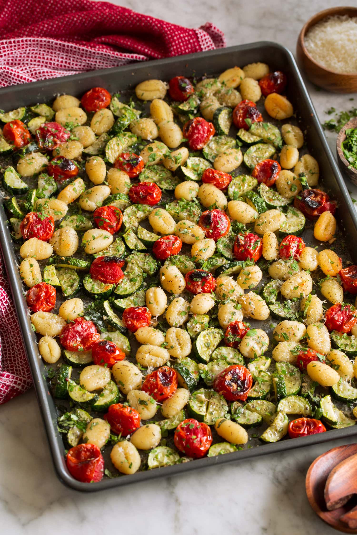 Baked gnocchi with vegetables on a dark baking sheet.