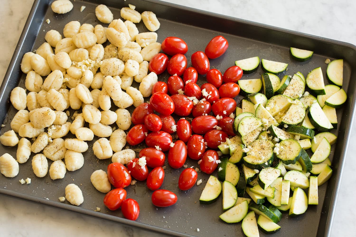 Gnocchi, tomatoes and zucchini on a baking sheet before tossing.