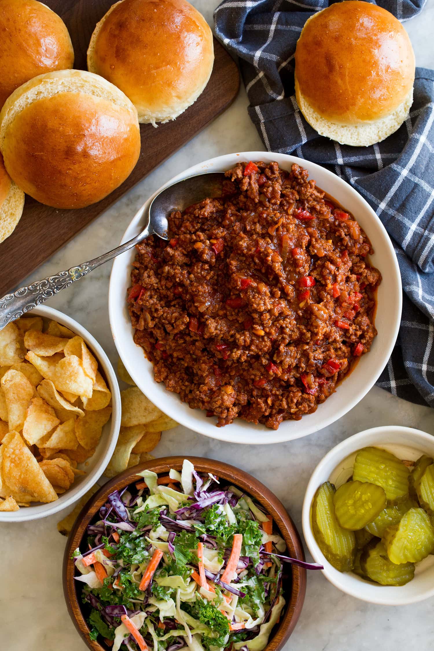 Sloppy joes filling in a bowl with buns and condiments to the side.