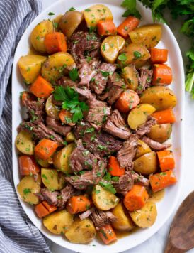 Slow Cooker Pot Roast with potatoes and carrots on a white oval serving platter set over marble.