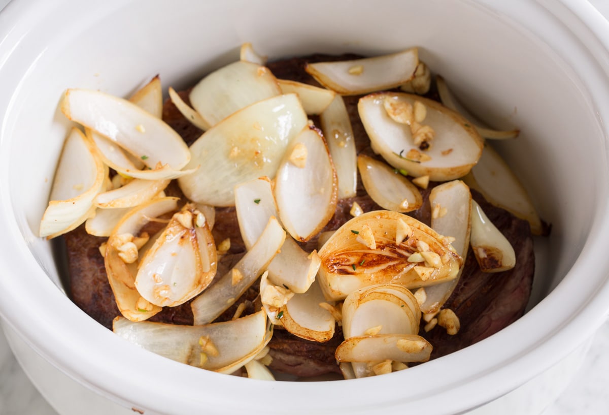 Adding sautéed onions and garlic over chuck roast in slow cooker.