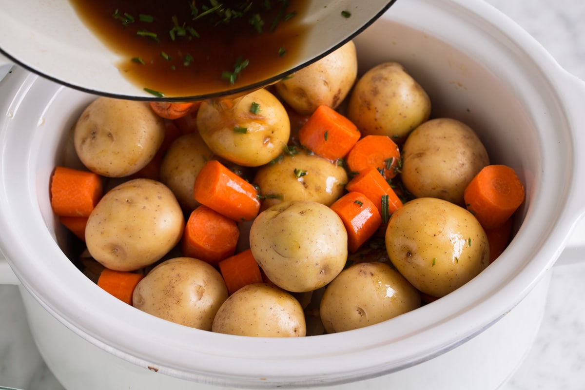 Adding potatoes and carrots over chuck roast and pouring over beef broth mixture.