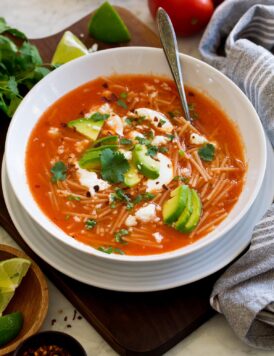 Sopa de fideo in a white soup bowl. Shown topped with avocado, cilantro, mexican crema, and queso fresco.