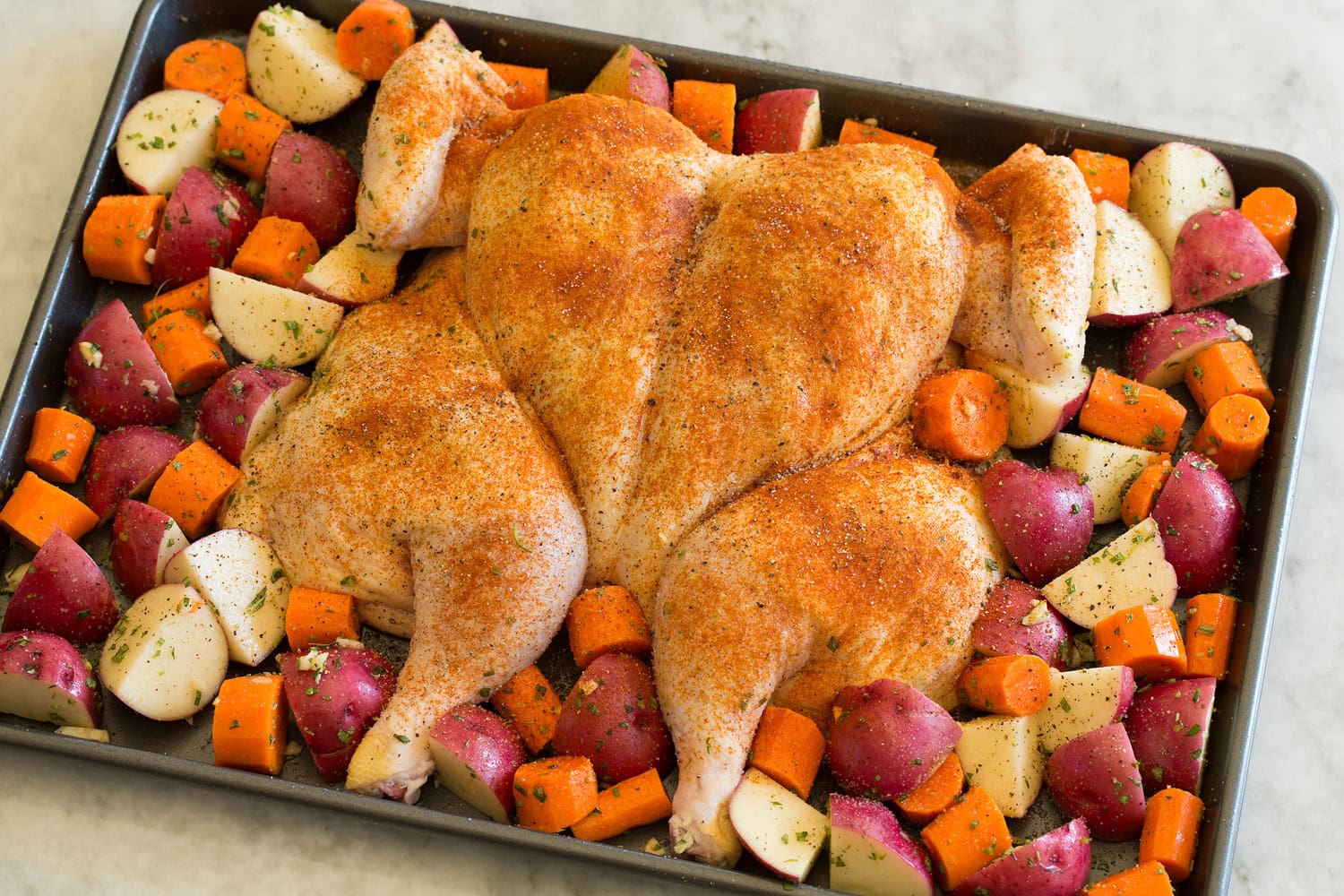 Spatchcock chicken and vegetables on a baking sheet shown before roasting.