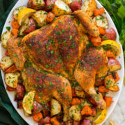 Spatchcock chicken with potatoes and carrots shown on a large oval white serving platter with lemons.