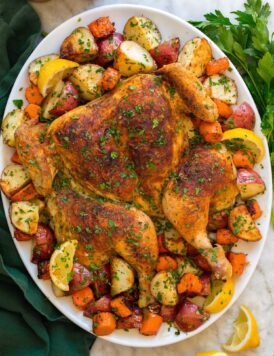 Spatchcock chicken with potatoes and carrots shown on a large oval white serving platter with lemons.