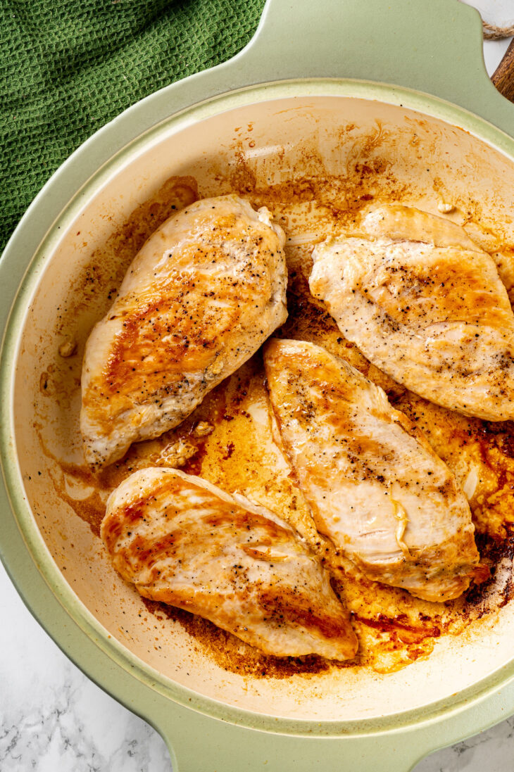 Overhead view of four browned chicken breasts in large skillet.