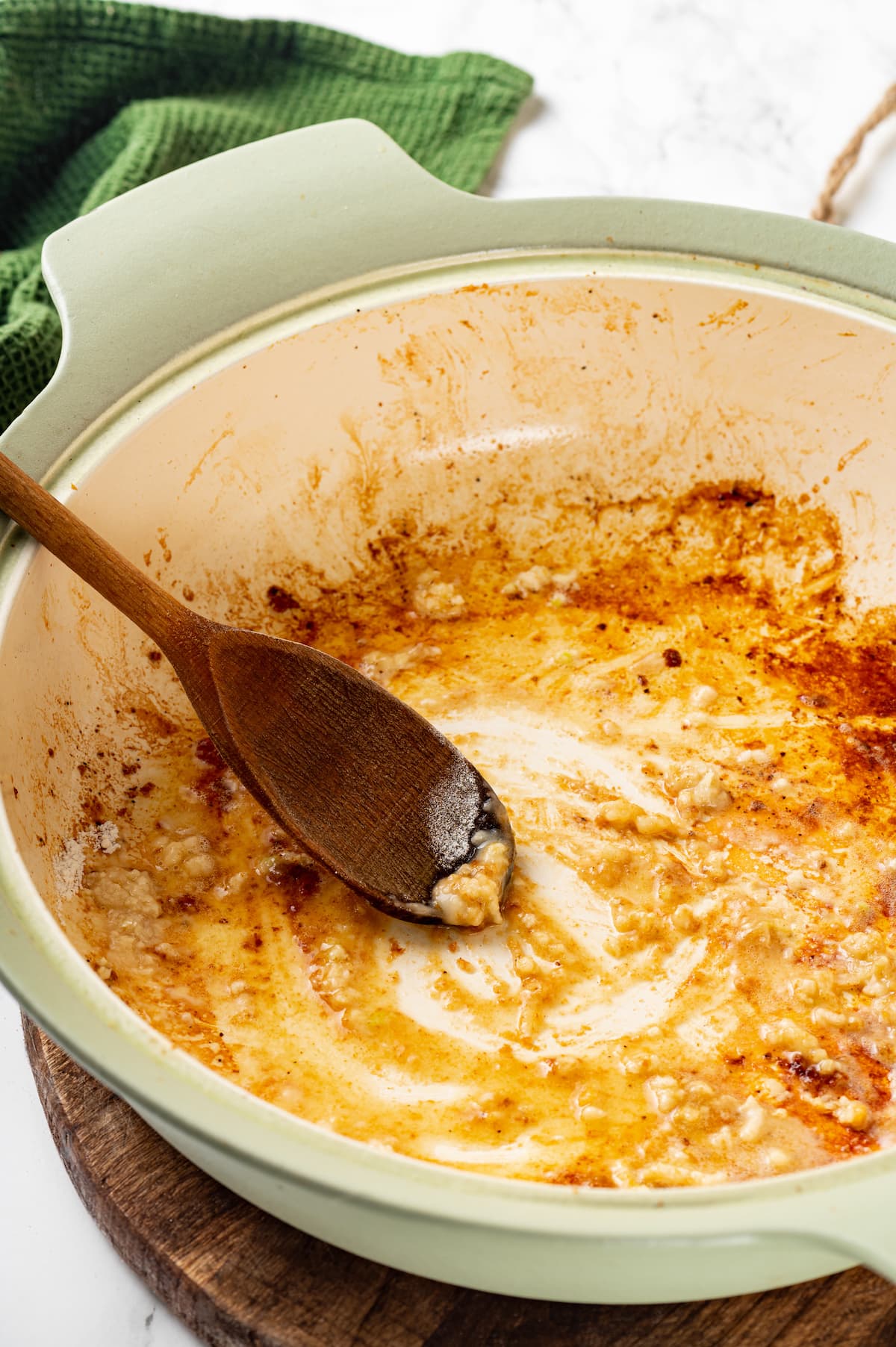 A wooden spoon is used to stir together butter and flour in a large skillet.