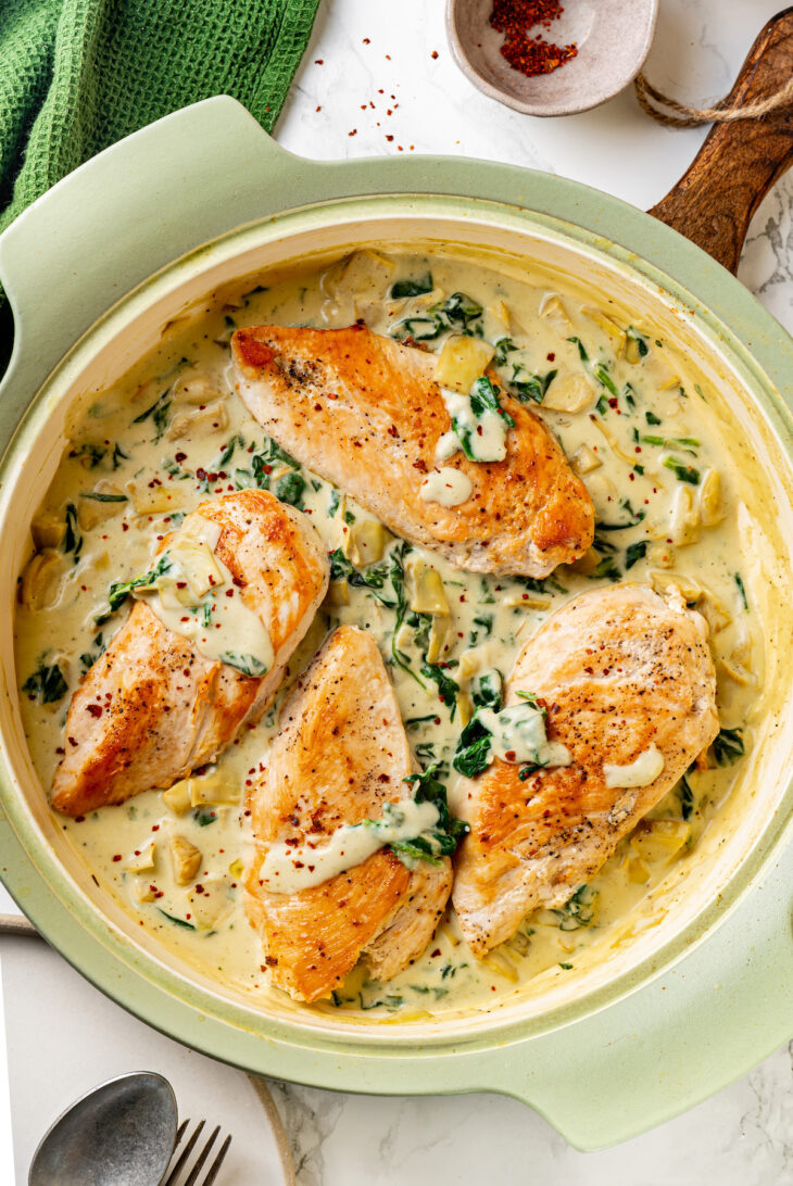 Overhead view of creamy spinach artichoke chicken in a large skillet.