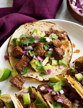 Single steak taco with avocado, cilantro and red onion shown close up.