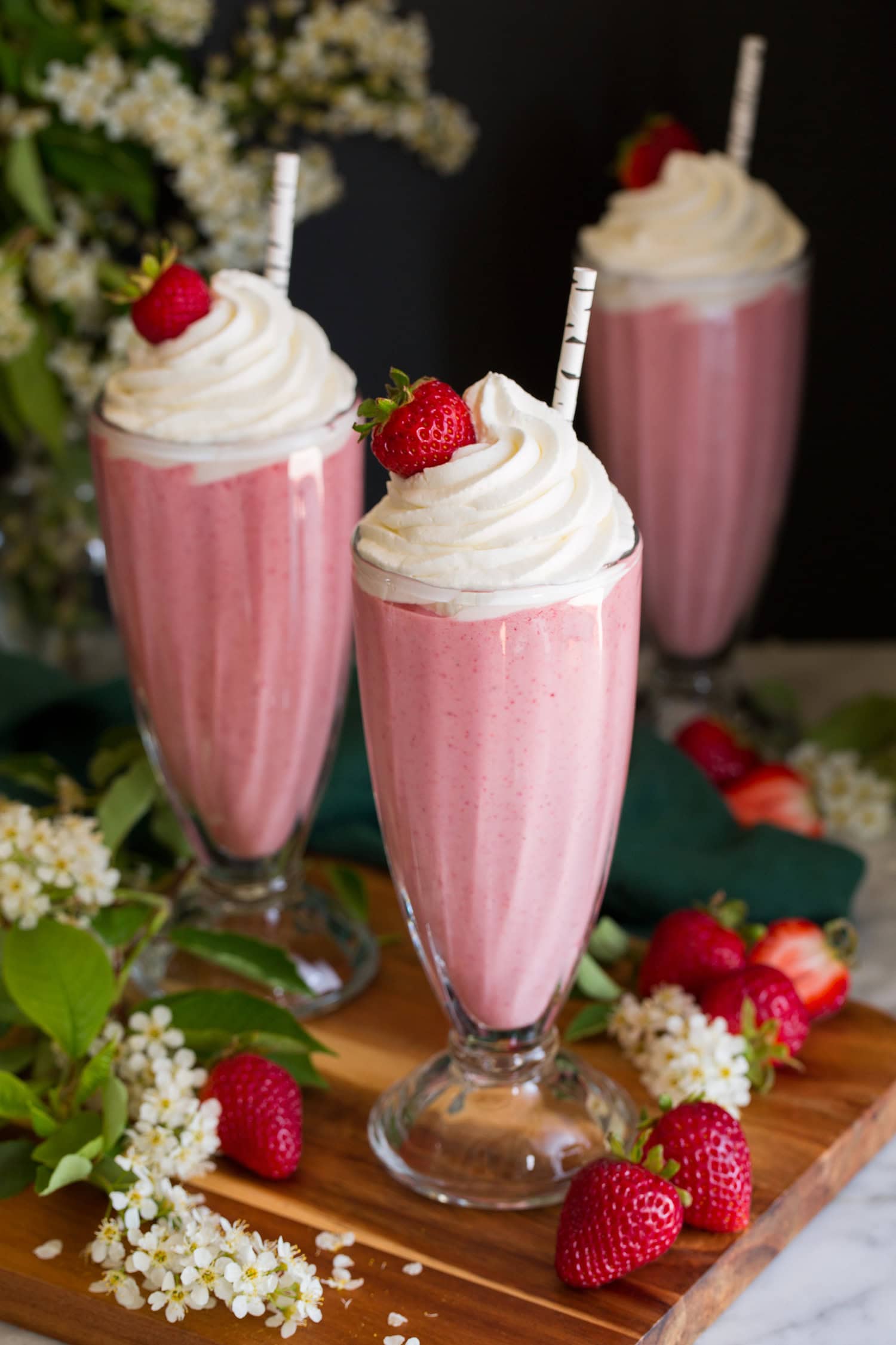 Three homemade strawberry milkshakes in tall glasses topped with whipped cream and strawberries.