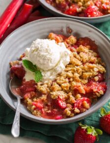 Single serving of strawberry rhubarb crisp shown in a grey bowl with ice cream on top.