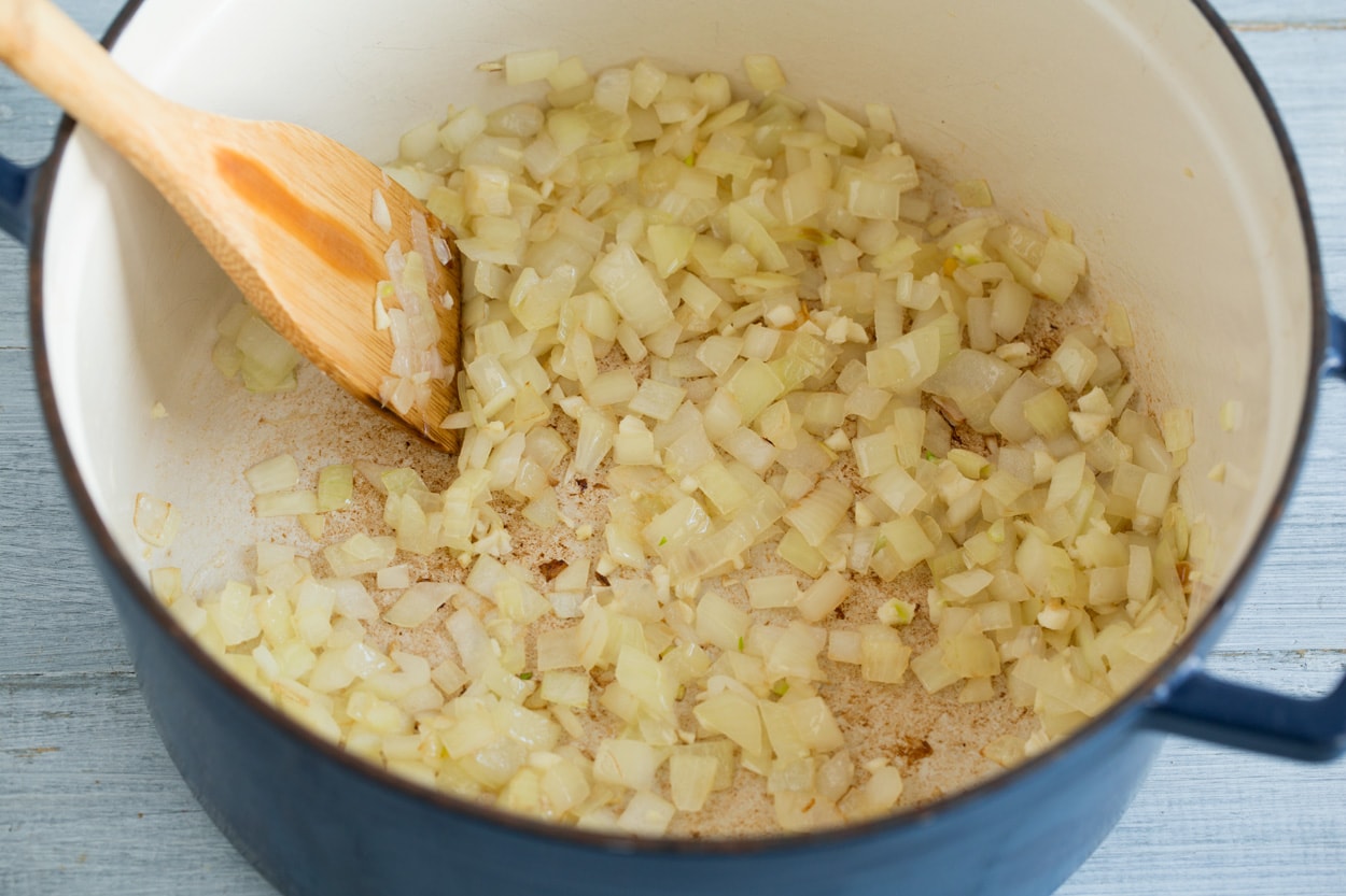 Showing how to make white chicken chili. Sauteing onion in oil in a large cast iron pot.