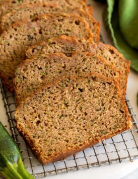 Close up image of sliced zucchini bread on a cutting board with a zucchini and green cloth set to the side.